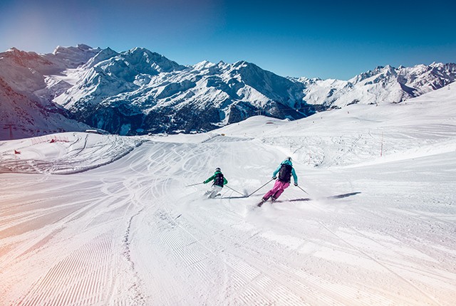 Valais, skiers on a bluebird day, mountains in background.